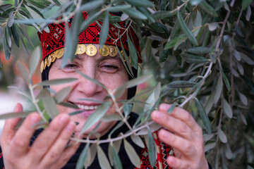 Portrait Of woman wearing palestinian traditional clothes in olive trees field holding branch in...