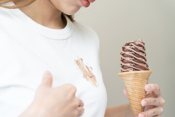 Cloth stain, disappointment asian young woman, girl eating melting ice cream in waffle cone on hot weather, hand show making chocolate cream drop on white t-shirt, spot dirty or smudge on clothes