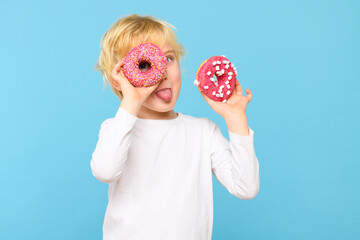 Boy with blond hair and freckles having fun with glazed donuts, sticking tongue out. Children and...