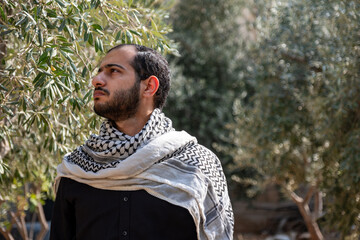 portrait for male wearing keffiyeh in olive tree field with black background and black shirts also...