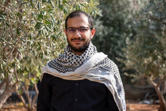 portrait for male wearing keffiyeh in olive tree field with black background and black shirts also with smile facial expression