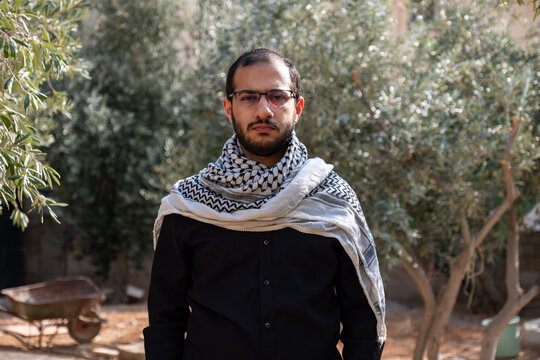 portrait for male wearing keffiyeh in olive tree field with black background and black shirts also with angry facial expression
