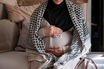 Palestinian pregnant female wearing keffiyeh on couch