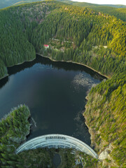 Aerial vertical panorama above Sadu lake during sunset. An arched dam made of concrete holds the water. the dam is built within the wilderness of Sadu Valley and Mountains. Carpathia, Romania - obrazy, fototapety, plakaty