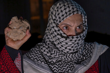 portrait for old woman holding stone which represents the only weapon against the occupation and...
