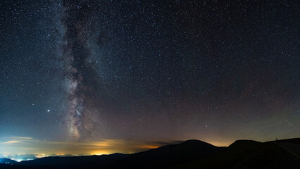 Milky way seen seen from the mountains, rising above urban city pollution in a summer night. Horizon is lit in orange color. Astrophotography with stars and constellations. Milky way's core is up.