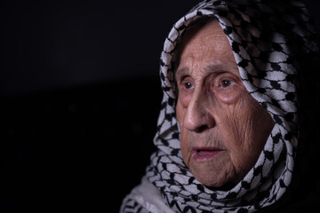 portrait of an old lady in dark background wearing white palestinian keffiyeh with smile on her face looking for freedom and hope to Right of Return for Palestinians