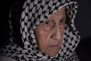 Portrait of old lady wearing white keffiyeh in dark with anger facial expression because of occupation and violence