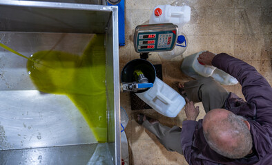 top view for An old Muslim man is engaged in the process of filling fresh olive oil into plastic gallons using a funnel and weighing scale in a pressing factory