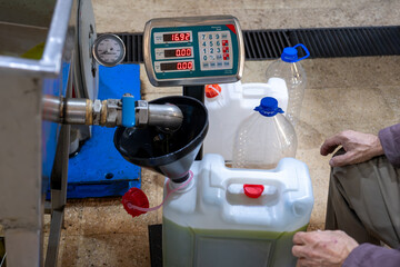 An old Muslim man is filling fresh olive oil into plastic gallons using a funnel and weighing scale in a pressing factory