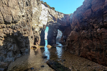 Obraz premium a rocky coastline with natural arches, calm waters reflecting sunlight, under a clear blue sky in asturias