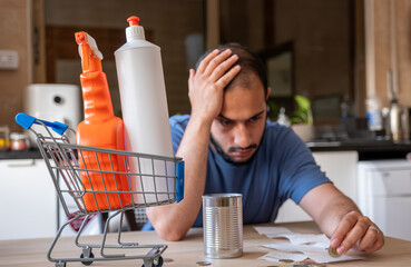 man sitting in the kitchen feeling frustrated due inflation and increase of daily needs supplies...