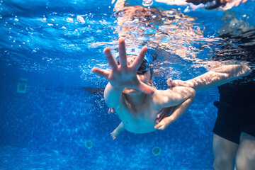 Little child swims underwater in swimming pool, happy active dives and has fun under water, kid...