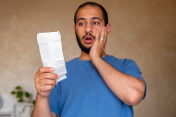 young bearded male holding reciepts in living room with emotion on his face