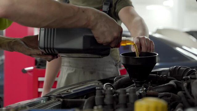 Auto mechanic replaces oil in car engine. Pouring fresh lubricant into motor at repair service station. Vehicle maintenance for efficiency. Hands work on auto parts, perform fluid change.