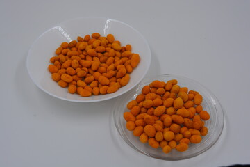 Fast food, snacks, salted battered peanuts and salted casing peanuts are located on white and clear glass plates.