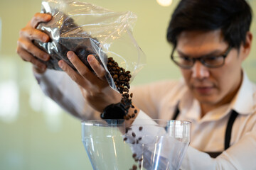Coffee grinder grinding roasted beans in powder. Asian male Barista makes espresso in cafe. Barista...