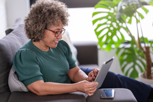 Beautiful middle-aged woman using a computer tablet to read a book and surf internet. Modern technologies used by elderly people. Mature woman using digital tablet at home