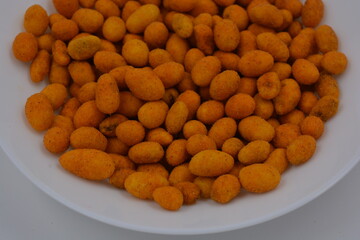 Quick food, snacks, salted battered peanuts and salted casings are arranged on a white glass plate. 