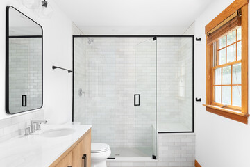 A beautiful luxury, modern bathroom with a light wood cabinet, walk-in shower with marble subway...