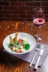 Salad with prosciutto, slices of grapes and cherry tomatoes, quail eggs on a plate and a glass of wine, dark and moody, top new