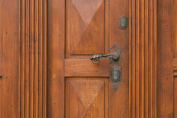 Vintage antique door handle on the old wooden door. Copper keyhole decorative element on weathered brown wood surface. Architecture in Hungary. Details of ornate orange colour entrance.