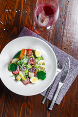 Salad with prosciutto, slices of grapes and cherry tomatoes, quail eggs on a plate and a glass of wine, dark and moody, top new