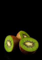 Closeup of a group of open green kiwis on black background, vertical, with copy space