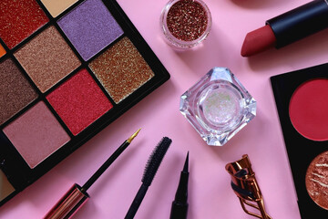 Various colorful make up products on pastel pink background. Top view.