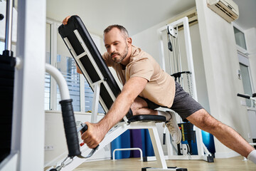bearded man in sportswear training on exercise machine in modern gym of kinesio center, recovery