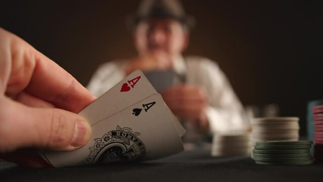 Poker game. A hand in the foreground lifts cards, revealing two aces. Opponent is blurred in the background. The table is laden with chips and cards, evoking a tense atmosphere. Camera 8K RAW.