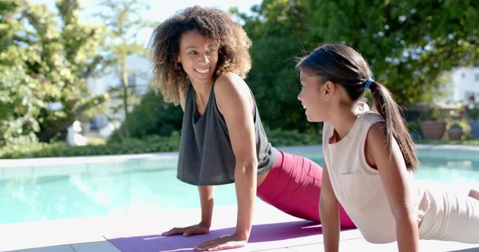 Happy biracial mother and daughter practicing yoga in sunny garden, copy space, slow motion