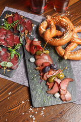 a set of deli meats for beer, dry-cured meat cut into pieces with cappers, on a slate board, beer glass, dark and moody, top new