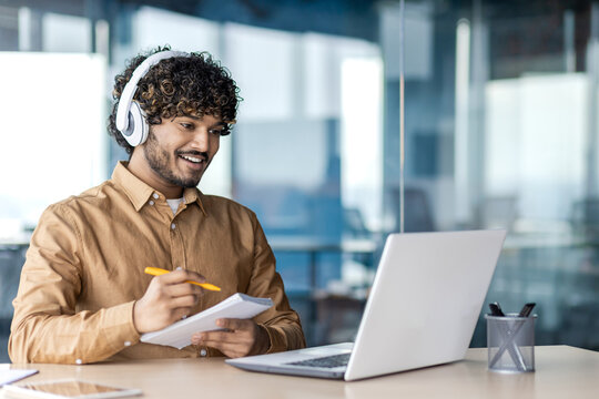 Businessman is studying inside the office, man is upgrading his qualifications, watching online video course, recording data, worker in headphones, talking, using video call.