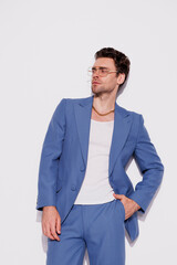 Fashionable man in trendy blue suit and white tank top posing near grey wall 