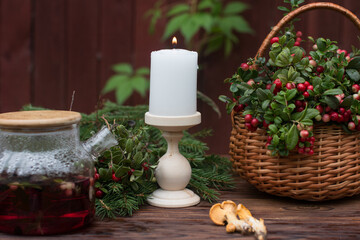 A bouquet of ripe red lingonberry berries in a wicker basket and a kettle of lingonberry tea. Forest orange chanterelle mushrooms
