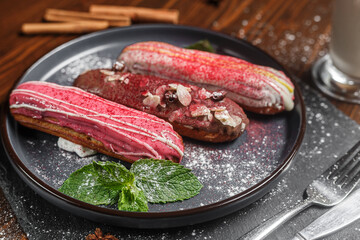 several eclairs lie on a black plate and a glass of cappuccino, dark and moody, top new