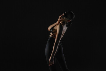 Young woman in black bodice and tights poses on black backlit studio background. Female dancer demonstrates elements of dance on high heels. Dance promo video concept.