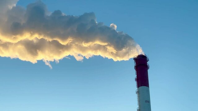 Real time footage featuring vapor emission from a tall power plant chimney against a backdrop of a clear sky. The billowing steam contrasts beautifully with the serene blue atmosphere, capturing the