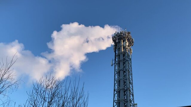 Real time footage featuring vapor emission from a tall power plant chimney against a backdrop of a clear sky. The billowing steam contrasts beautifully with the serene blue atmosphere, capturing the