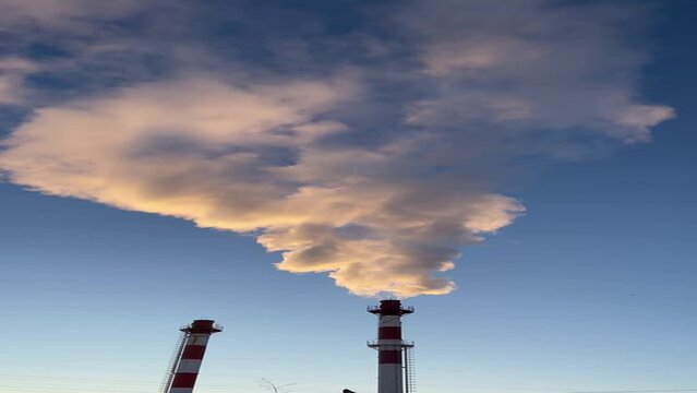Real time footage featuring vapor emission from a tall power plant chimney against a backdrop of a clear sky. The billowing steam contrasts beautifully with the serene blue atmosphere, capturing the