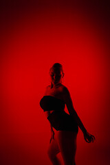 Silhouette female dancer in black shorts and top dancing on high heels. Young woman poses gracefully and shows off slender flexible body in dark studio with red light.