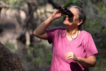 Senior woman using binoculars during vacation post retirement.