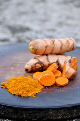 closeup the bunch sliced orange color turmeric with powder on the wooden soft focus natural grey brown background.