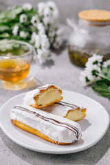 Fresh tasty eclair on white plate and cup of tea