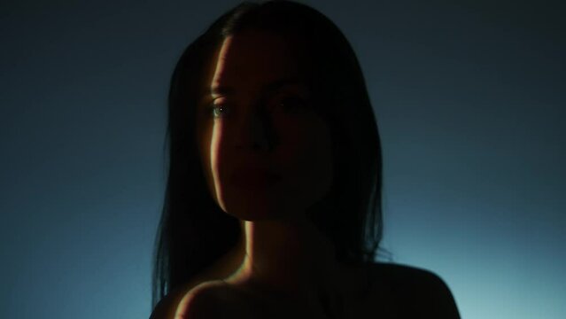 Portrait of female model in studio. Silhouette of appealing woman face close up posing on white low light background, selective ray of light.