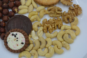 Healthy and wholesome food, snacks, lots of natural nuts: cashews, almonds, walnuts, hazelnuts and biscuits placed on a white glass plate.