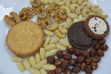 Fototapeta na wymiar Healthy and wholesome food, snacks, lots of natural nuts: cashews, almonds, walnuts, hazelnuts and biscuits placed on a white glass plate.