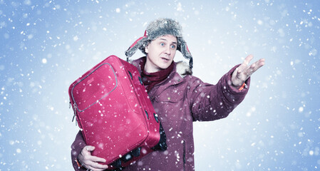 A man in winter clothes, who was late for transport, holds a red suitcase in his hands, making a...