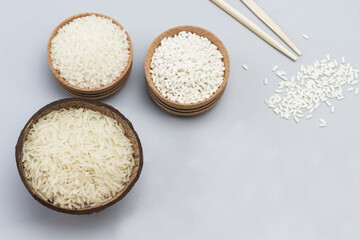 Three types of white rice in wooden bowls and coconut shells. Wooden spoon with rice and sticks
